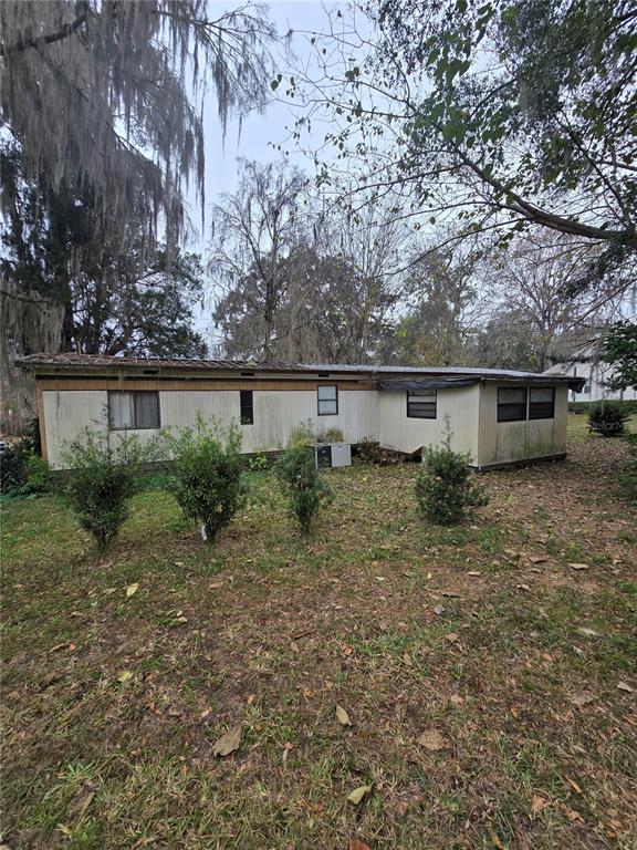 A single-story mobile home with light-colored siding sits on a grassy lot with trees — 9374 CR 657, BUSHNELL, FL