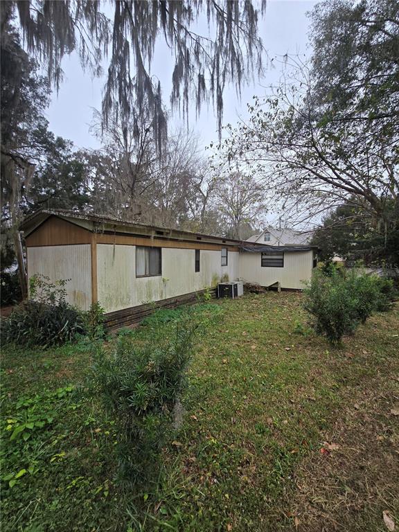 A weathered mobile home with light-colored siding sits on a grassy lot with trees — 9374 CR 657, BUSHNELL, FL