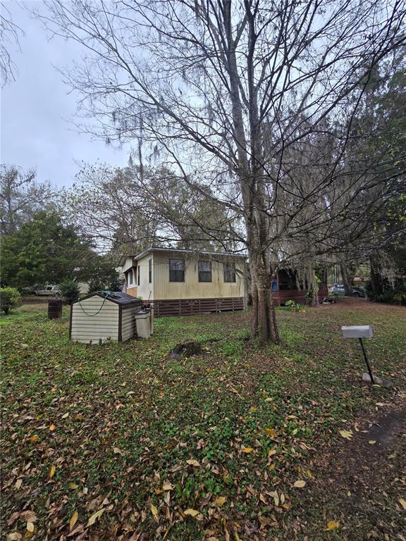 A small, light-colored mobile home sits on a grassy lot with a shed and trees — 9374 CR 657, BUSHNELL, FL