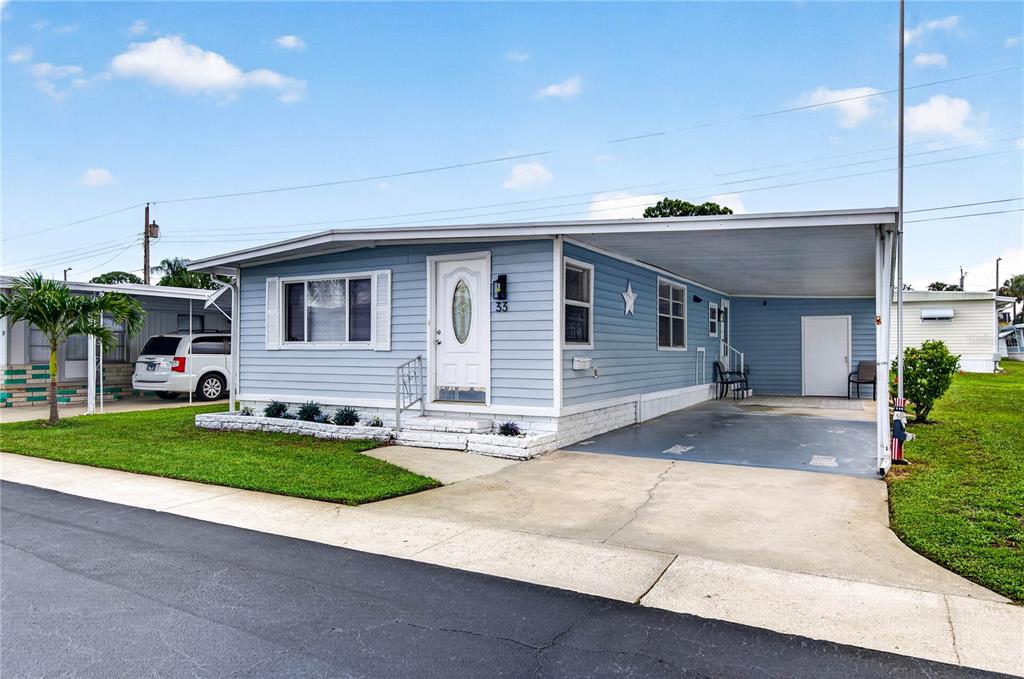 A light blue manufactured home features a front porch, a carport, and a small lawn — 2000 E BAY DRIVE UNIT 33, LARGO, FL