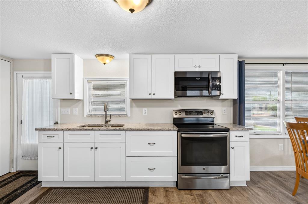 A kitchen featuring white cabinets, granite countertops, stainless steel appliances, and wood-look flooring — 2000 E BAY DRIVE UNIT 33, LARGO, FL
