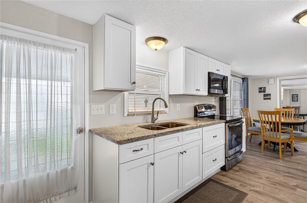 A kitchen with white cabinets, granite countertops, stainless steel appliances, and a dining area nearby — 2000 E BAY DRIVE UNIT 33, LARGO, FL