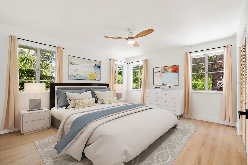 A bedroom features a bed with blue accents, white furniture, a ceiling fan, and large windows — 2002 VIRGINIA DRIVE, BRADENTON, FL