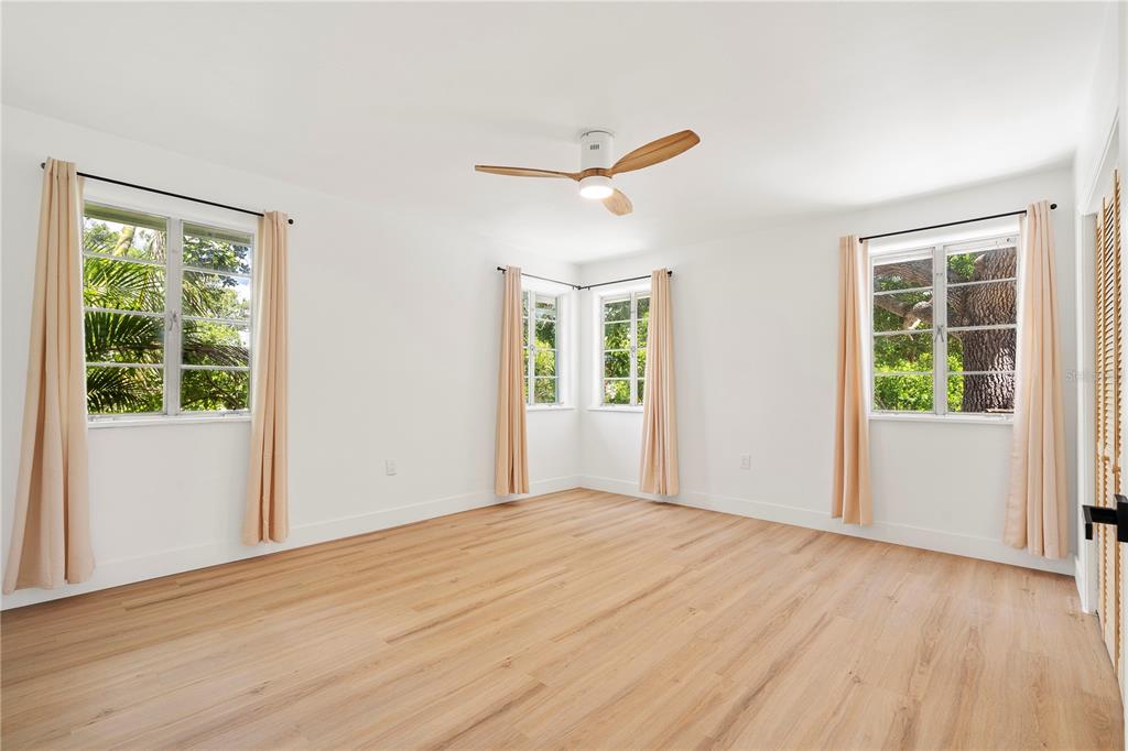 A bright bedroom features white walls, light wood flooring, a ceiling fan, and multiple windows — 2002 VIRGINIA DRIVE, BRADENTON, FL