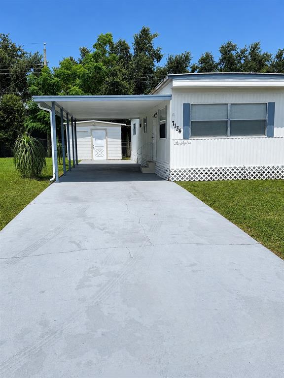 A white mobile home features a concrete driveway and an attached carport leading to a shed — 7134 LOFTY DRIVE, PORT RICHEY, FL