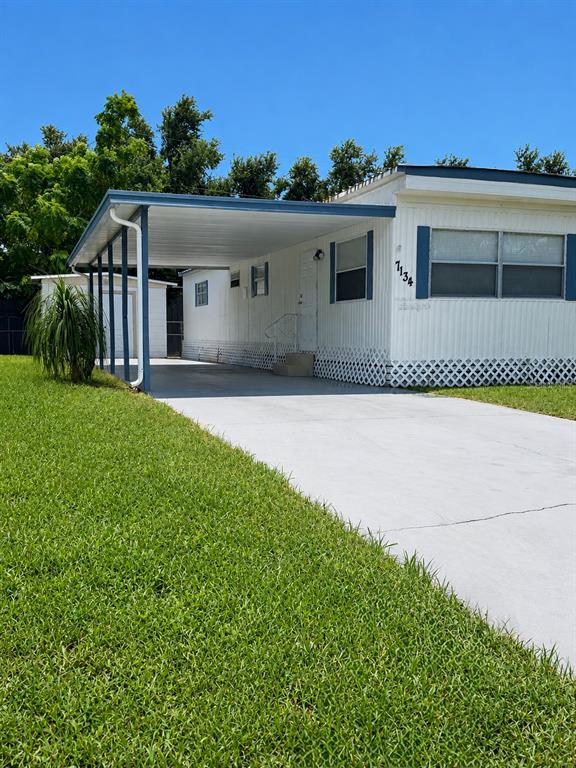 A white mobile home features a metal carport, a concrete driveway, and a small storage shed — 7134 LOFTY DRIVE, PORT RICHEY, FL