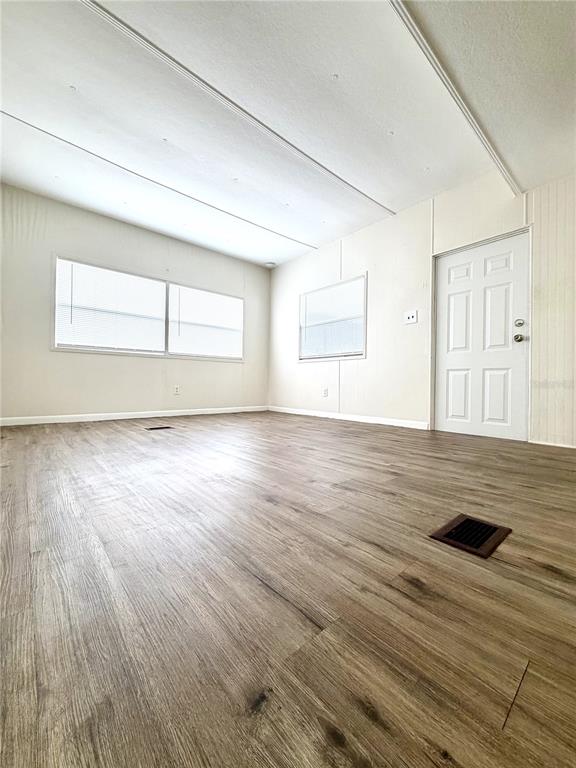 An empty room features light-colored walls, wood-look flooring, two windows, and a white door — 7134 LOFTY DRIVE, PORT RICHEY, FL