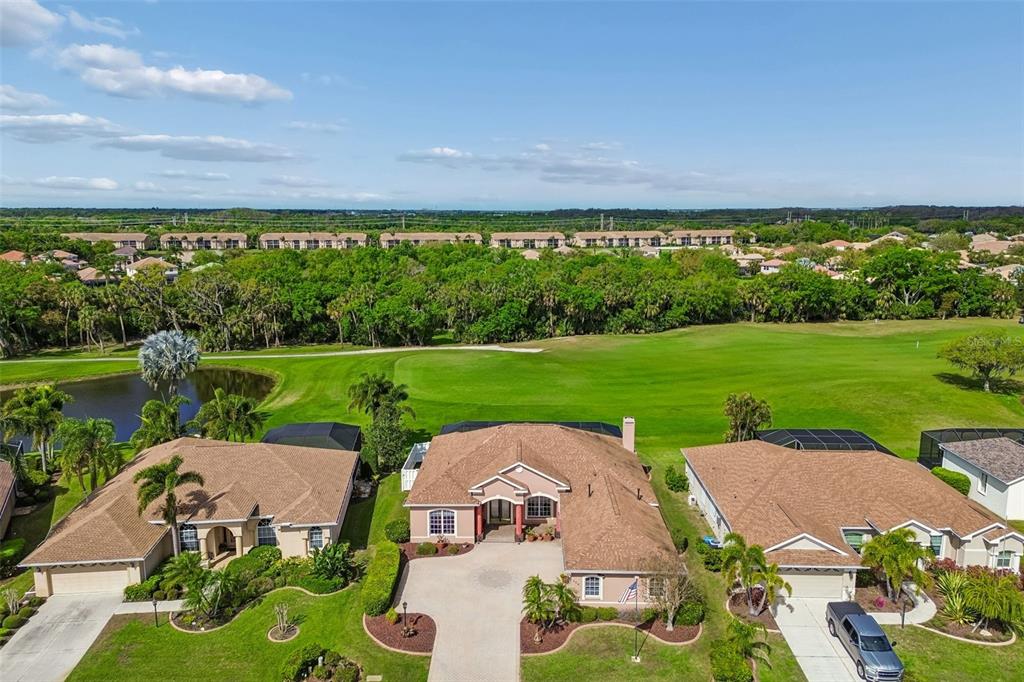 An aerial view shows three suburban houses with brown roofs overlooking a large green golf course — 566 PLANTERS MANOR WAY, BRADENTON, FL