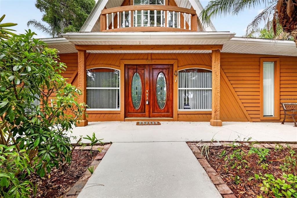 A wooden house exterior features a double front door, a balcony, and a concrete walkway — 507 LAKESHORE DRIVE, EUSTIS, FL