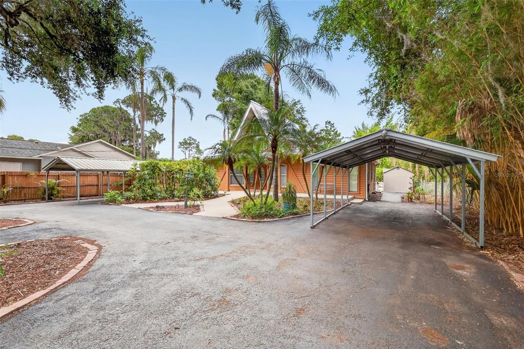 A house with a metal carport and a paved driveway surrounded by trees and landscaping — 507 LAKESHORE DRIVE, EUSTIS, FL
