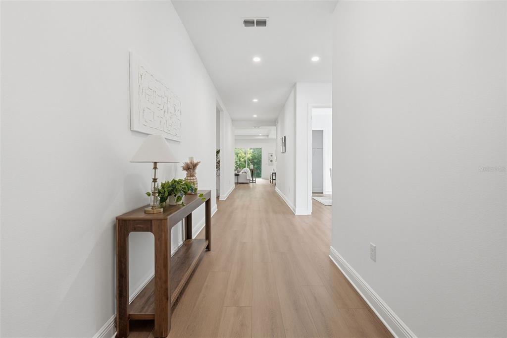 A long hallway with light wood flooring, white walls, and a wooden console table — 1664 STONECLIFF DRIVE, APOPKA, FL