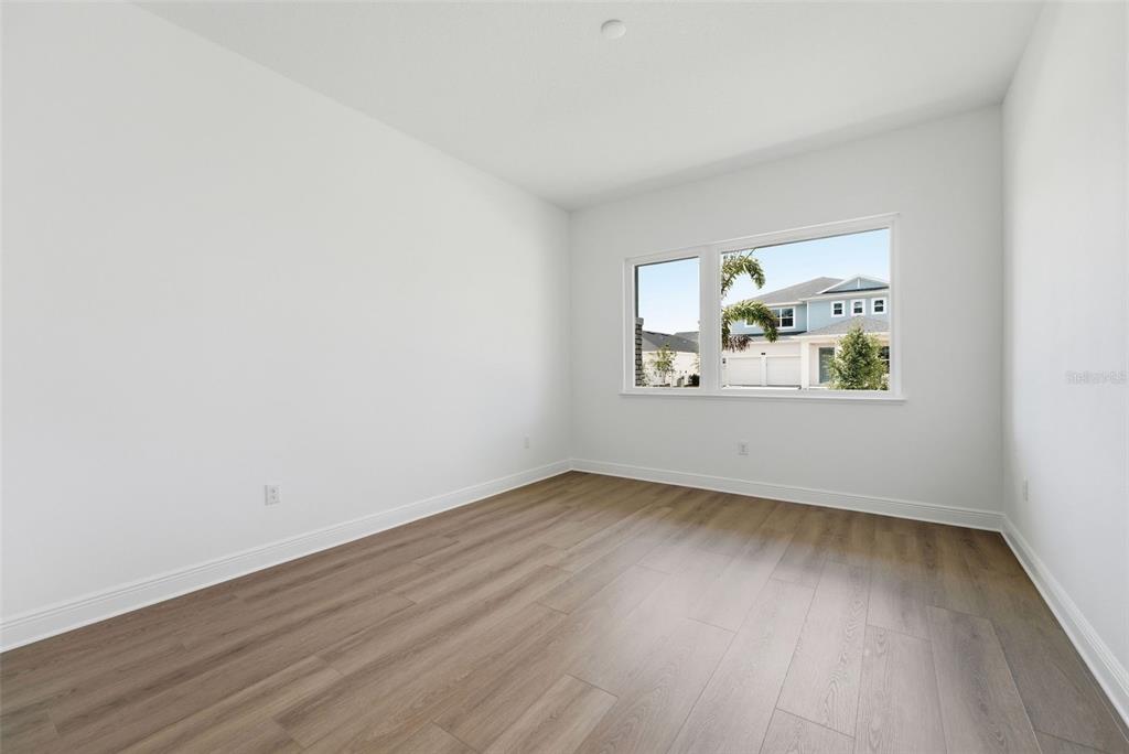 An empty room with white walls, wood-look flooring, and a window overlooking a neighboring house — 1664 STONECLIFF DRIVE, APOPKA, FL