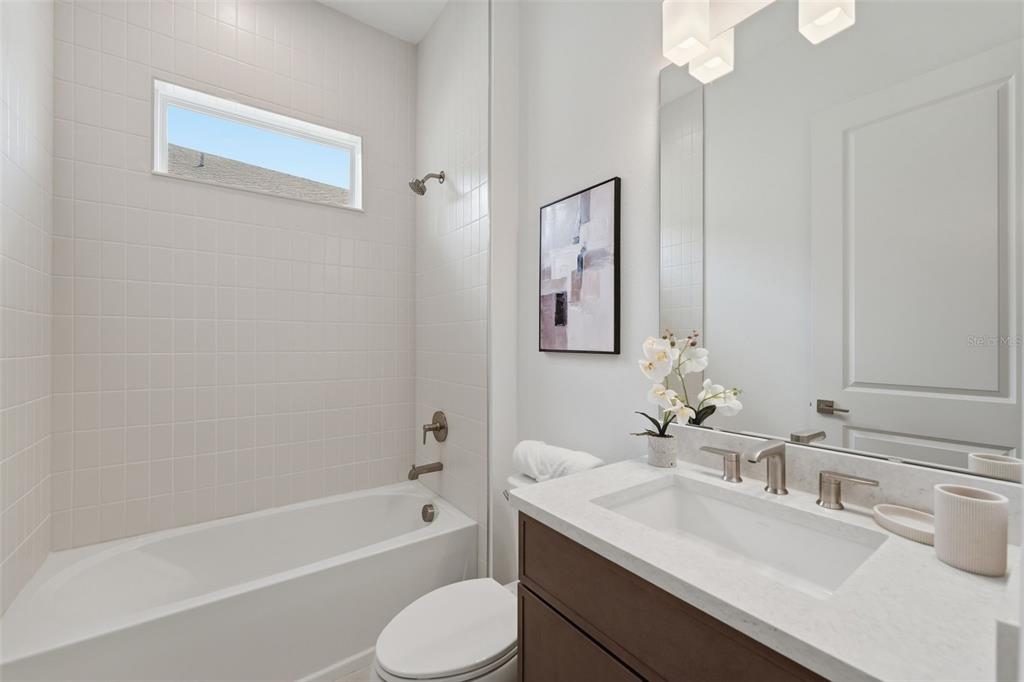 A modern bathroom features a white bathtub, tiled shower wall, vanity, and a rectangular mirror — 1664 STONECLIFF DRIVE, APOPKA, FL