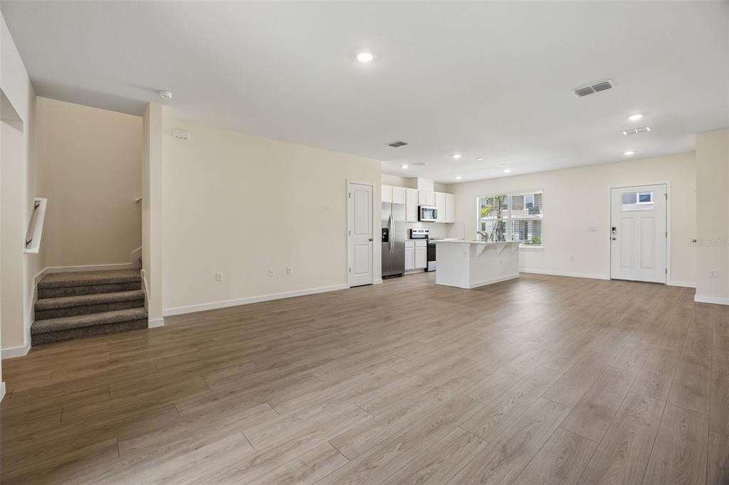 An open-concept living area features light wood-look flooring, a kitchen island, and carpeted stairs — 16576 BARBOURS CREEK WAY, WINTER GARDEN, FL