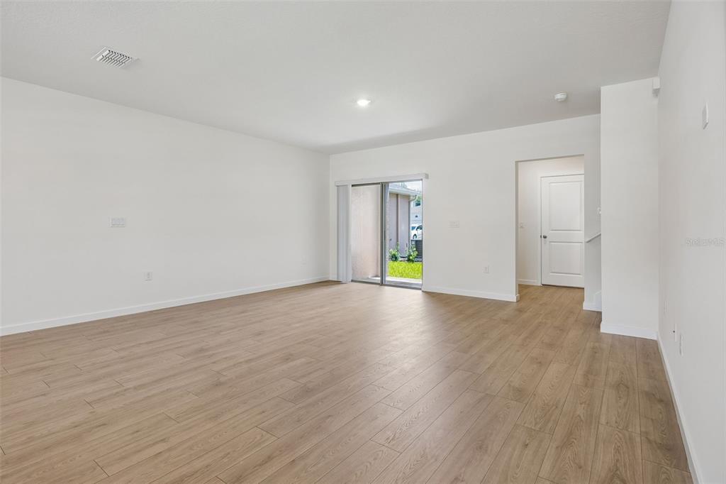 An empty living room with white walls, light wood-look flooring, and a sliding glass door — 16576 BARBOURS CREEK WAY, WINTER GARDEN, FL