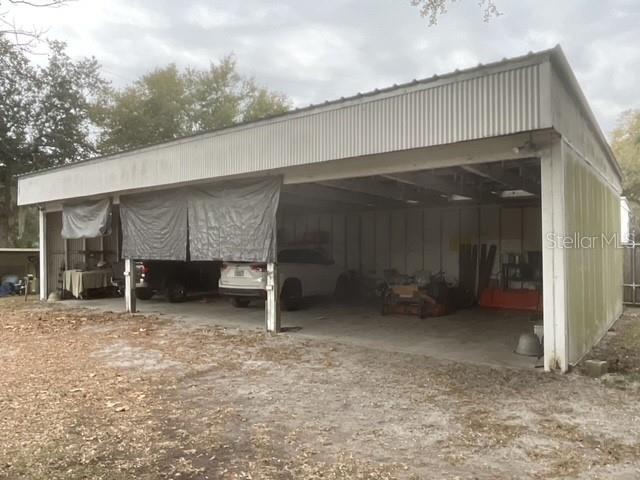 A large, open-sided metal carport structure sits on a dirt lot with vehicles parked inside — 32420 COUNTY ROAD 473, LEESBURG, FL