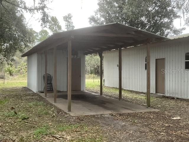 A metal-roofed carport stands adjacent to a white metal-sided building on a grassy lot — 32420 COUNTY ROAD 473, LEESBURG, FL