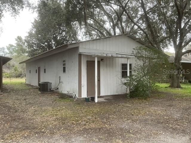 A single-story building with white metal siding and a brown door stands under large trees — 32420 COUNTY ROAD 473, LEESBURG, FL