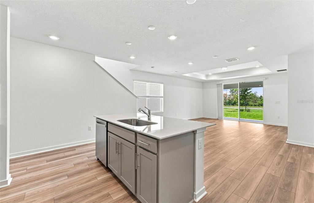 A modern kitchen features gray cabinets, a white quartz island with seating, and stainless appliances — 7923 PALM PARADISE PLACE, PARRISH, FL