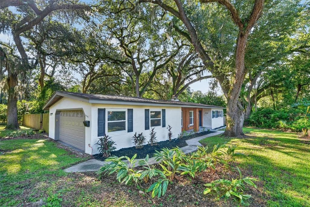 A single-story house with a garage, white stucco walls, and large oak trees in front — 1202 ORANOLE ROAD, MAITLAND, FL