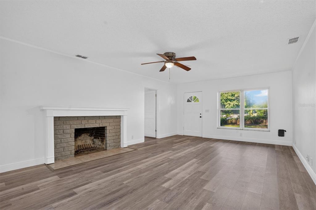 A living room features a brick fireplace, wood-look flooring, a ceiling fan, and white walls — 1202 ORANOLE ROAD, MAITLAND, FL