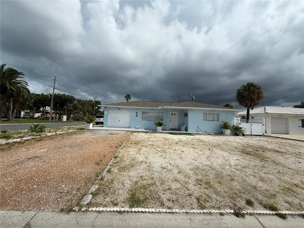 A light blue single-story house with a gravel front yard under a cloudy sky — 59 45TH AVENUE, ST PETE BEACH, FL