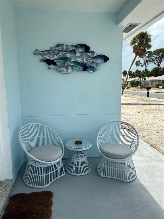 A light blue porch features two white wicker chairs, a small table, and fish wall decor — 59 45TH AVENUE, ST PETE BEACH, FL