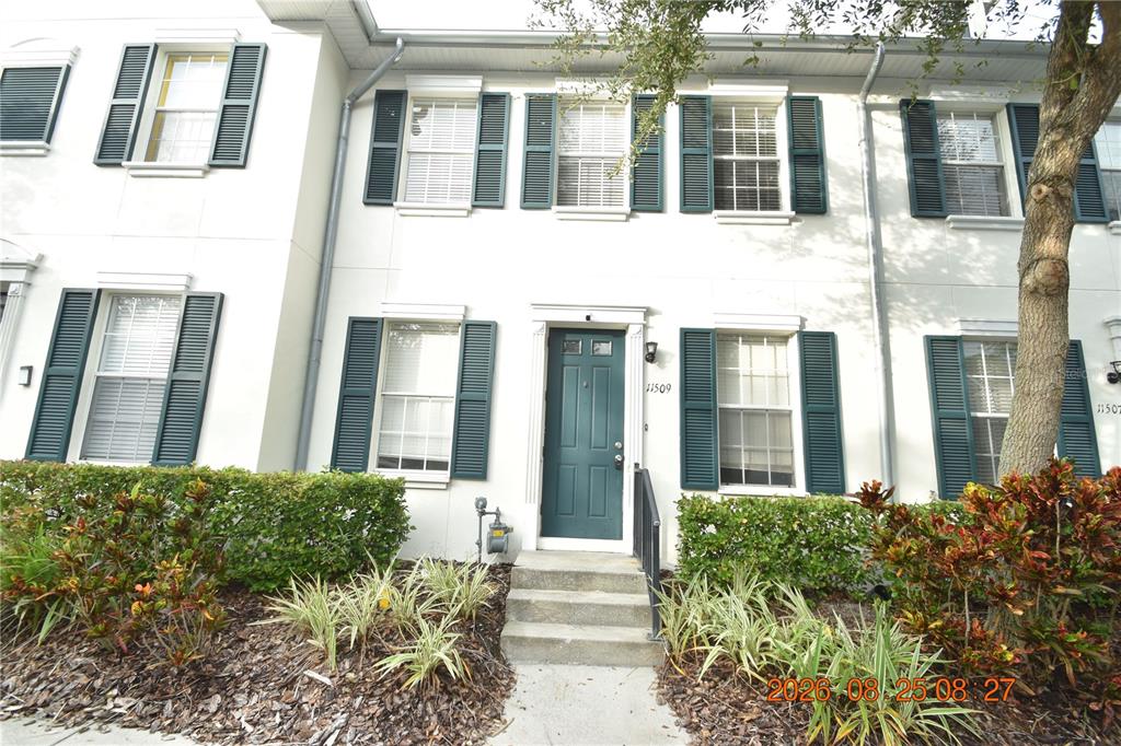 A two-story townhouse exterior features a dark green front door, white shutters, and landscaping — 11509 FOUNTAINHEAD DRIVE, TAMPA, FL