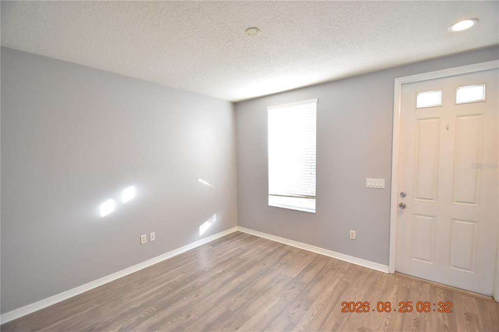 An empty room with gray walls, wood-look flooring, a window with blinds, and a white door — 11509 FOUNTAINHEAD DRIVE, TAMPA, FL