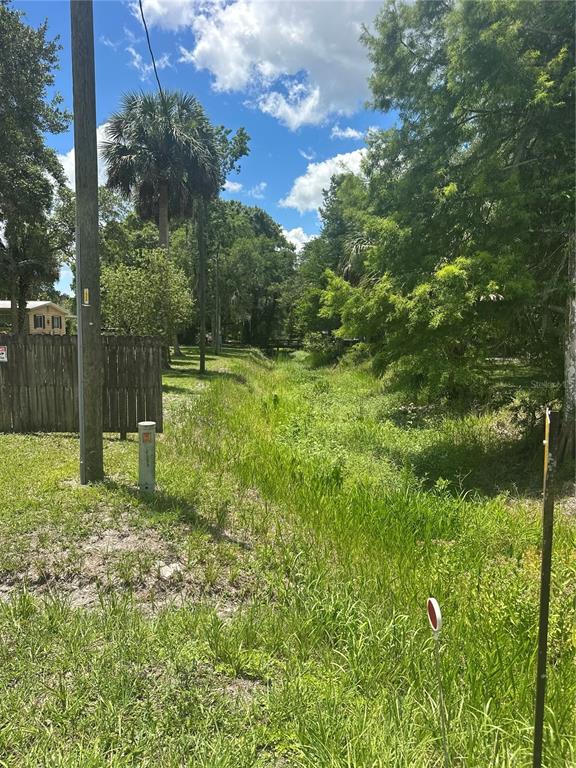 A grassy drainage ditch runs between a wooden fence and trees under a blue sky — 10828 E FREDDY STREET, INVERNESS, FL