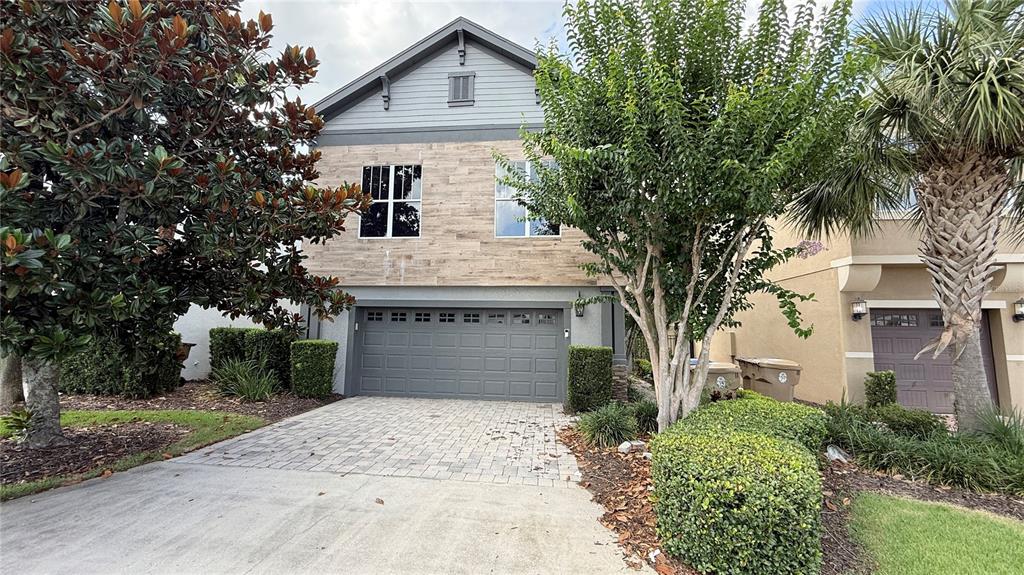 A two-story house with a stone-veneer facade, a gray garage door, and a paved driveway — 7810 WHITEMARSH WAY, REUNION, FL