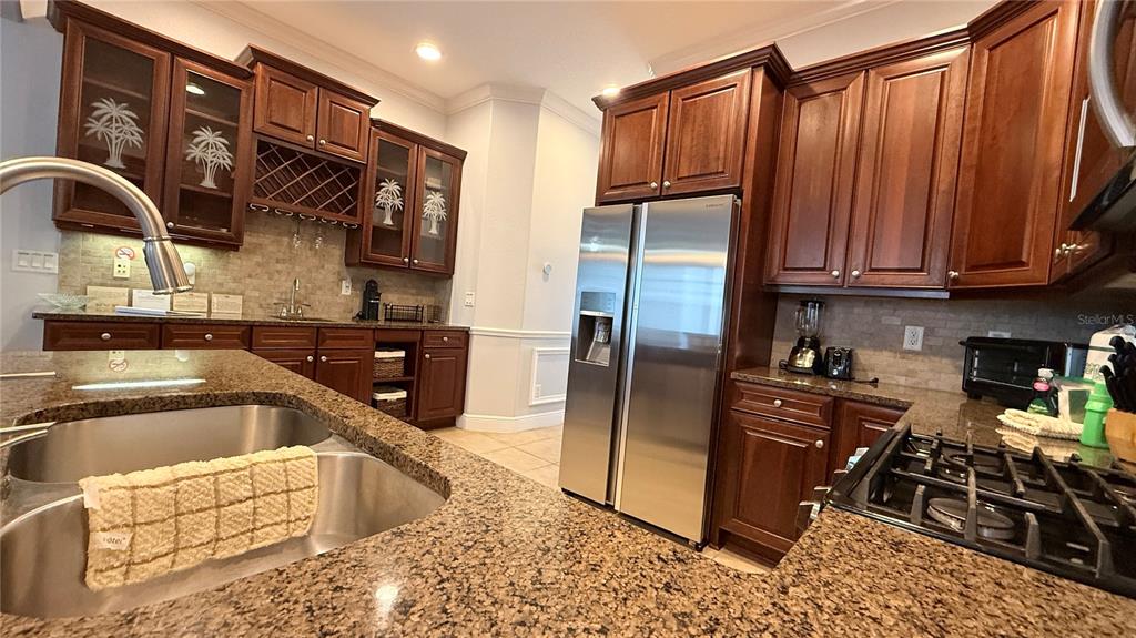 A kitchen features dark wood cabinets, granite countertops, stainless steel appliances, and a double sink — 7810 WHITEMARSH WAY, REUNION, FL