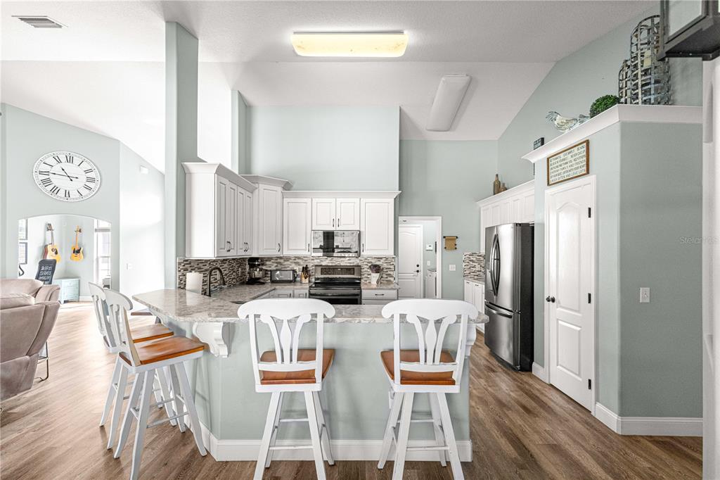 A kitchen features white cabinets, granite countertops, a breakfast bar with stools, and light-colored walls — 5430 COUNTY ROAD 125, WILDWOOD, FL