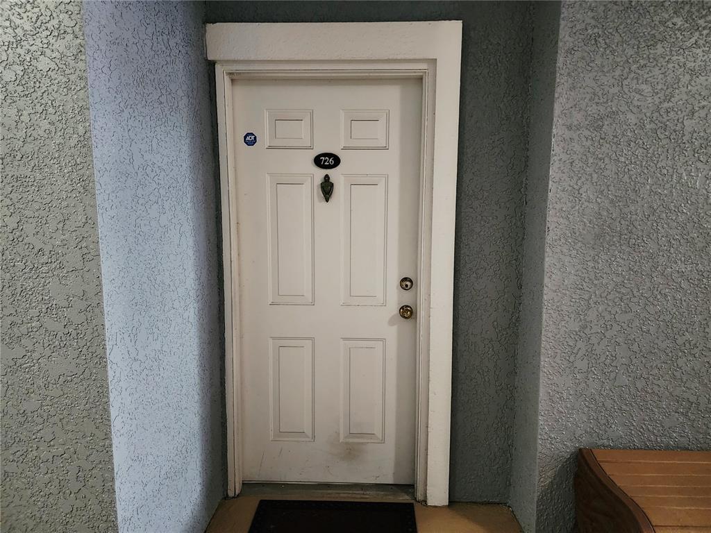 A white front door with a number plate and door knocker sits in a stucco entryway — 3621 CONROY ROAD UNIT 726, ORLANDO, FL