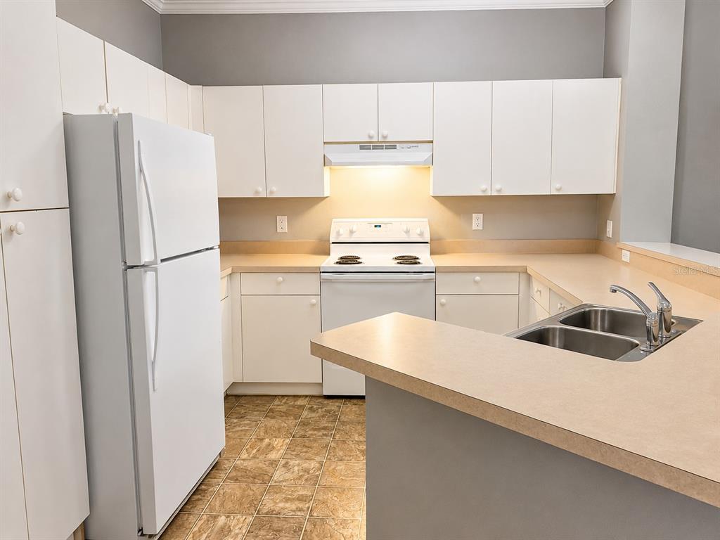 A kitchen features white cabinets, a white refrigerator, a white stove, and tan countertops — 3621 CONROY ROAD UNIT 726, ORLANDO, FL