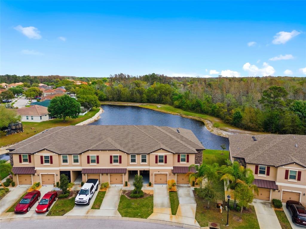 An aerial view shows a multi-unit townhouse complex with a pond and wooded area behind — 8606 REEDVILLE STREET, NEW PORT RICHEY, FL