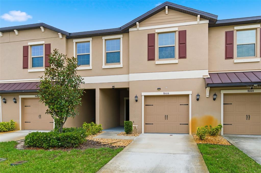 A tan two-story townhouse with a brown garage door and a small front yard — 8606 REEDVILLE STREET, NEW PORT RICHEY, FL