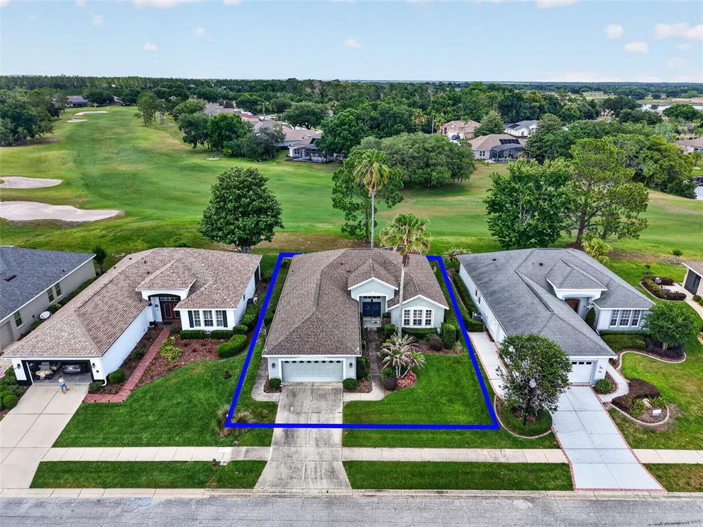 An aerial view shows a single-story house with a garage and lawn facing a golf course — 8011 PINE HOLLOW DRIVE, MOUNT DORA, FL