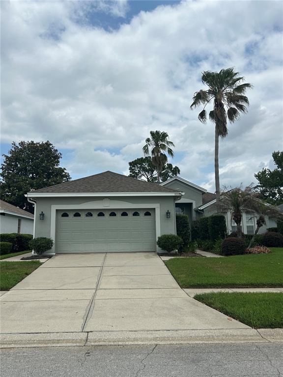 A single-story house with a two-car garage, light green siding, and palm trees in front — 8011 PINE HOLLOW DRIVE, MOUNT DORA, FL