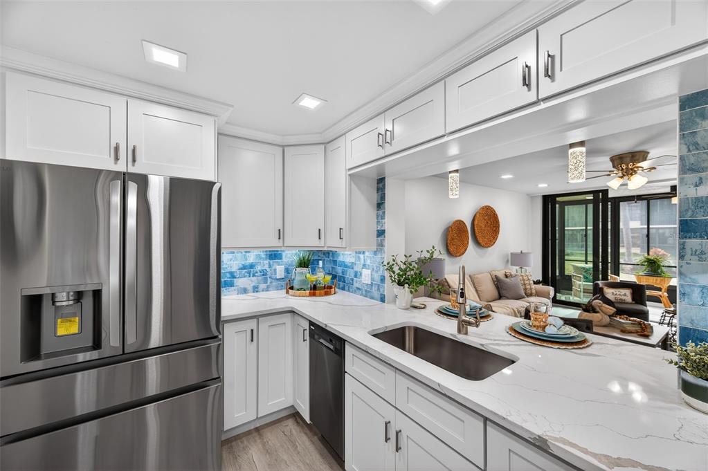 A kitchen with white cabinets, stainless steel appliances, and a blue tiled backsplash — 19701 GULF BOULEVARD UNIT 120, INDIAN SHORES, FL