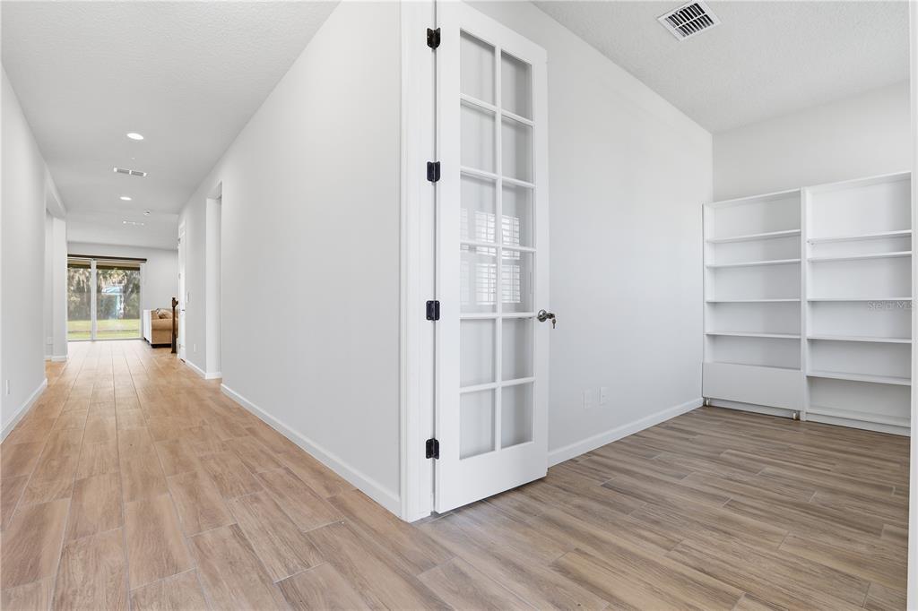 A room with wood-look tile flooring, white walls, built-in shelving, and a glass-paneled French door — 3610 ARBORDALE LOOP, SANFORD, FL