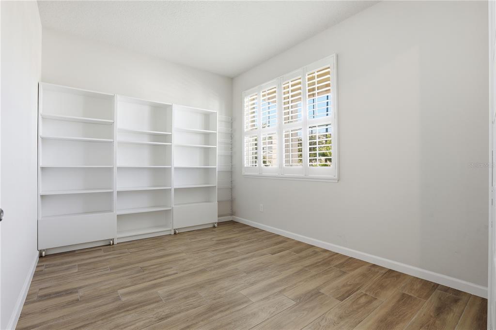A room with light-colored walls, wood-look tile flooring, white bookshelves, and plantation shutters — 3610 ARBORDALE LOOP, SANFORD, FL