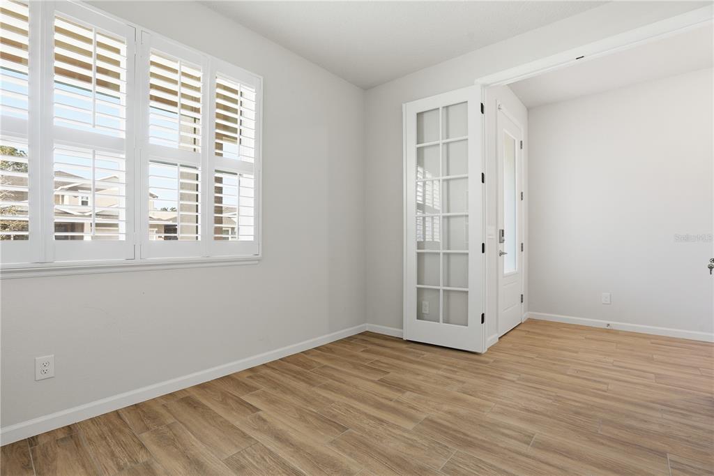 An empty room features light-colored walls, wood-look tile flooring, plantation shutters, and French doors — 3610 ARBORDALE LOOP, SANFORD, FL