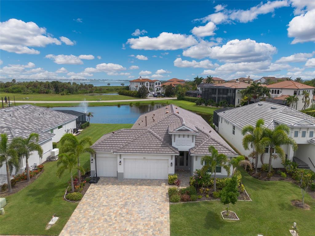 An aerial view shows a single-story house with a tiled roof, paver driveway, and pond — 5504 TITLE ROW DRIVE, BRADENTON, FL