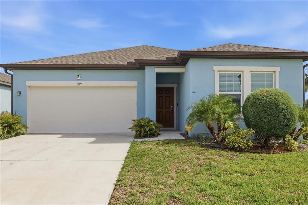 A light blue single-story house features a two-car garage, a brown door, and landscaping — 1121 ANCHOR BEND DRIVE, RUSKIN, FL
