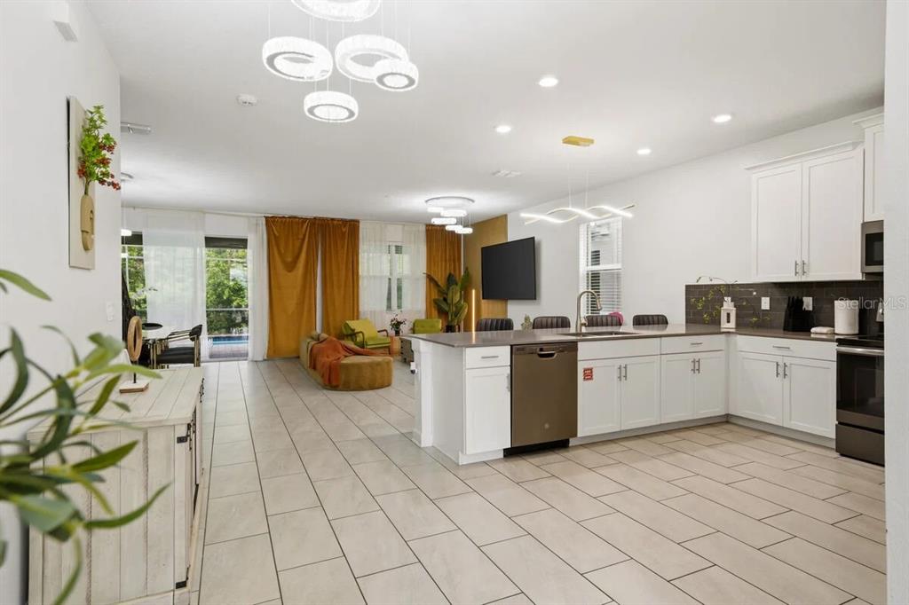 An open-concept kitchen and living area features white cabinetry, tile flooring, and gold curtains — 2703 BOOKMARK DRIVE, KISSIMMEE, FL