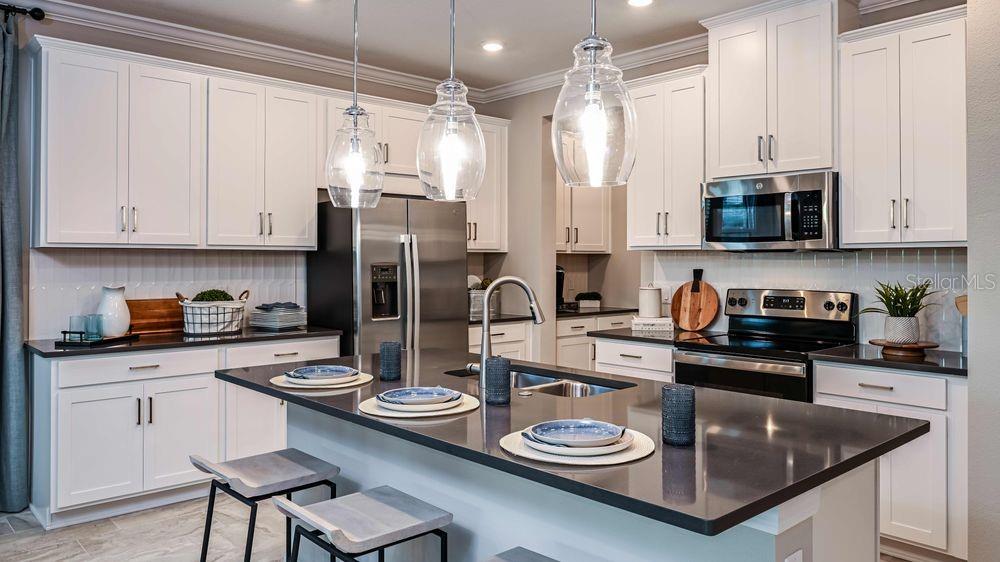 A modern kitchen features white cabinetry, dark countertops, a central island, and three glass pendant lights — 15532 FOXTAIL LANE, NOKOMIS, FL