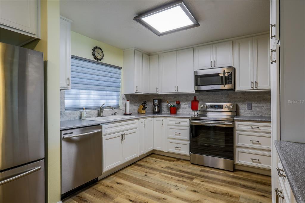 A kitchen with white cabinets, stainless steel appliances, a tiled backsplash, and wood-look flooring — 260 S CENTRAL AVENUE, UMATILLA, FL