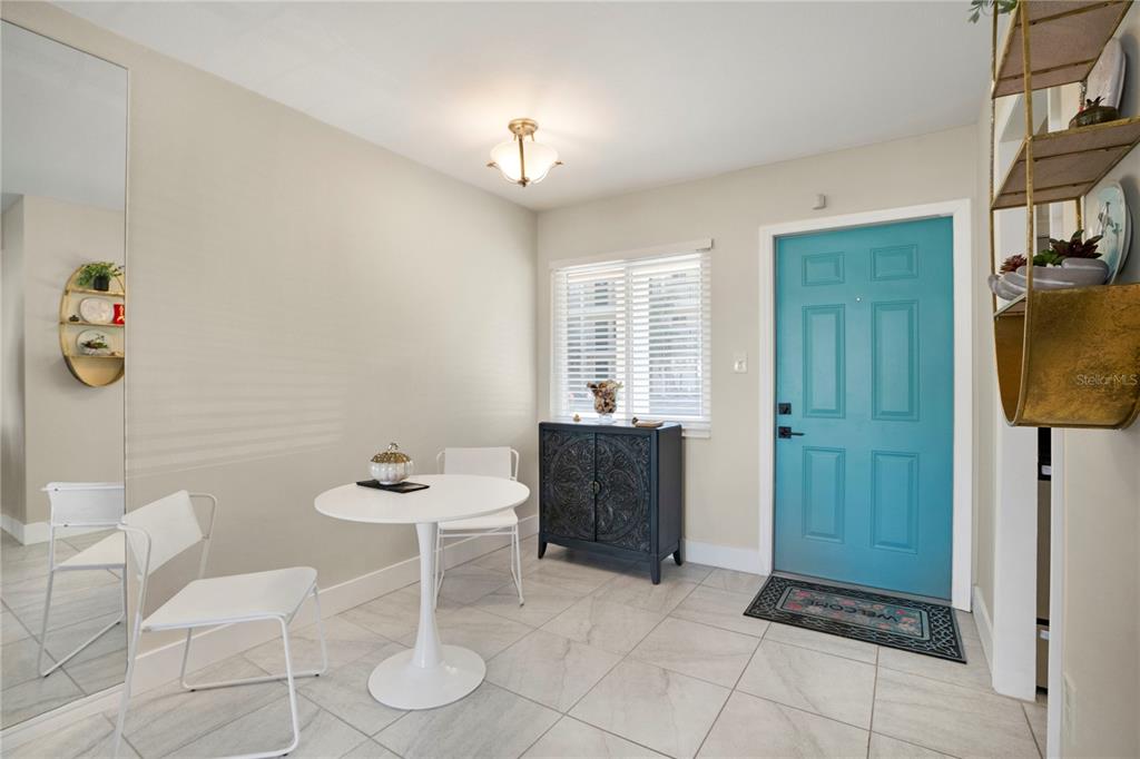 A dining area features a white pedestal table, two chairs, and a bright blue door — 2211 SUNSET DRIVE UNIT E3, BRADENTON, FL