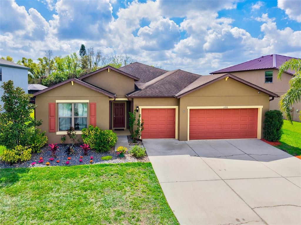 A single-story house with a brown exterior, red garage doors, and a concrete driveway — 11216 58TH STREET CIRCLE E, PARRISH, FL